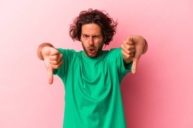 Pembe fırında izole edilmiş genç beyaz bir adam baş parmağını aşağı gösteriyor ve hoşlanmadığını ifade ediyor..