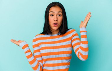 Mavi arka planda izole edilmiş genç Venezuelalı kadın avuç içinde fotokopi alanı tutuyor, el üstünde tutuyor. Şaşırmış ve mutlu..