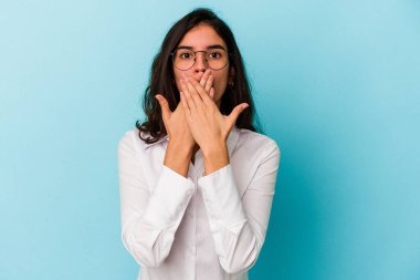 Mavi arka planda izole edilmiş genç beyaz kadın şok olmuş, ağzı ellerle kaplanmış, yeni bir şey keşfetmeye hevesli..