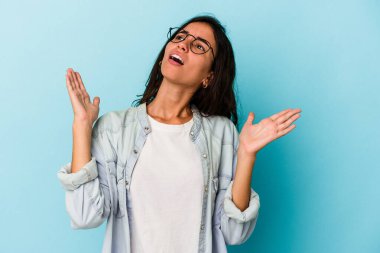 Mavi arka planda izole edilmiş genç beyaz kadın gökyüzüne haykırıyor, yukarı bakıyor, hayal kırıklığına uğramış..