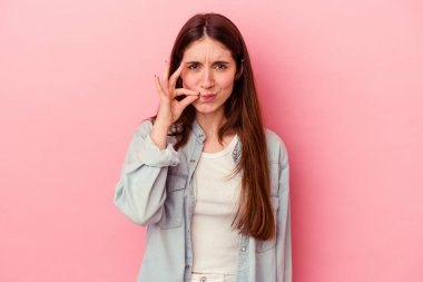 Pembe arka planda izole edilmiş genç beyaz kadın parmakları dudaklarında bir sır saklıyor..