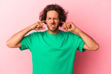 Genç, beyaz bir adam pembe bir bakkalda izole edilmiş parmaklarıyla kulaklarını kapatıyor, gürültülü bir ortam yüzünden stresli ve çaresiz.