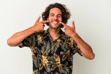 Beyaz arka planda izole edilmiş genç beyaz adam gülümsüyor, parmaklarını ağıza doğrultuyor..