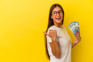 Elinde banknotlar tutan beyaz bir kadın. Sarı arka planda izole edilmiş. Baş parmak uzakta, gülen ve kaygısız..