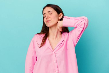 Genç beyaz kadın mavi arka planda izole edilmiş. Stres yüzünden boynu ağrıyor. Masaj yapıyor ve elle dokunuyor..