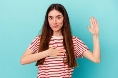 Beyaz bir kadın mavi arka planda izole edilmiş yemin ediyor, elini göğsüne koyuyor..