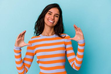 Kafkasyalı genç bir kadın mavi arka planda izole edilmiş. Elinde avuç içi olan bir şeyle kameraya sunuyor..