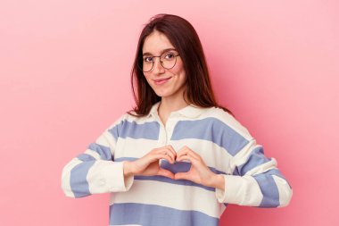 Gülümsüyor ve elleriyle kalp şeklini gösteriyor..