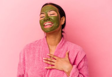 Genç Venezuelalı kadın, pembe arka planda izole edilmiş bornoz ve yüz maskesi takıyor..