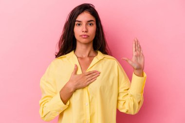 Pembe arka planda izole edilmiş genç beyaz kadın yemin ediyor, elini göğsüne koyuyor..