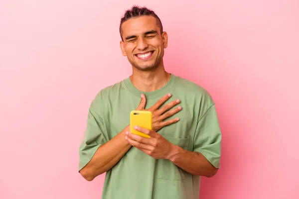 Młody Wenezuelczyk Trzymający Telefon Komórkowy Różowym Tle Śmieje Się Głośno — Zdjęcie stockowe