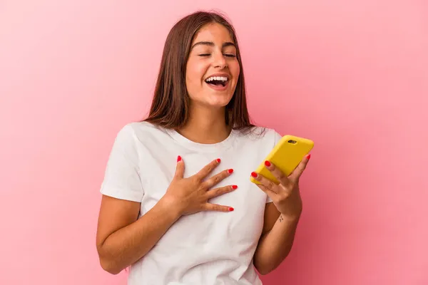 年轻的高加索女人拿着一部粉色背景的手机大声笑着把手放在胸前 — 图库照片