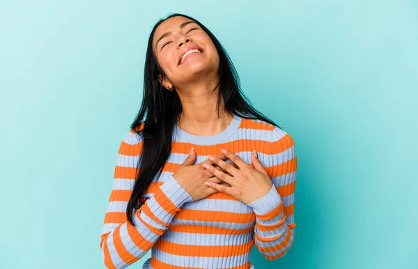 若いベネズエラの女性は青の背景に隔離された笑い大声で手を保つ胸 — ストック写真