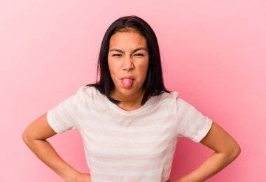 Genç Venezuelalı bir kadın pembe arka planda izole edilmiş komik ve dost canlısı bir dil kullanıyor..