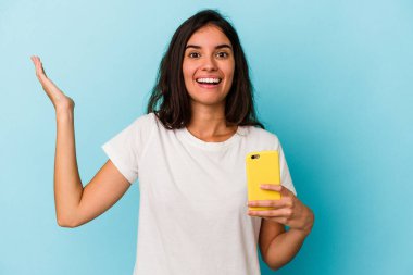 Mavi arka planda cep telefonu tutan beyaz bir kadın hoş bir sürpriz yaşıyor, heyecanlı ve el kaldırıyor..