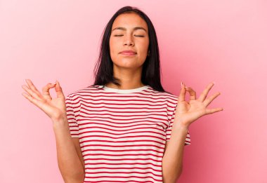 Genç Venezuelalı kadın pembe arka planda izole edilmiş yoğun bir günün ardından dinleniyor, yoga yapıyor..