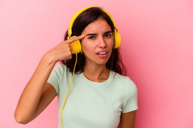 Pembe arka planda izole edilmiş müzik dinleyen beyaz bir kadın işaret parmağıyla yaptığı hayal kırıklığı jestini gösteriyor..