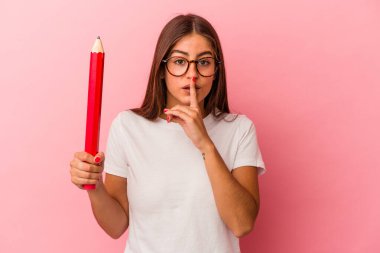 Pembe arka planda büyük bir kalem tutan genç beyaz kadın bir sır saklıyor ya da sessizlik istiyor..