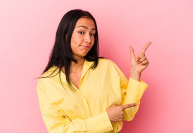 Pembe arka planda izole edilmiş genç Venezuelalı kadın işaret parmağıyla fotokopi alanını işaret ederek şok oldu..