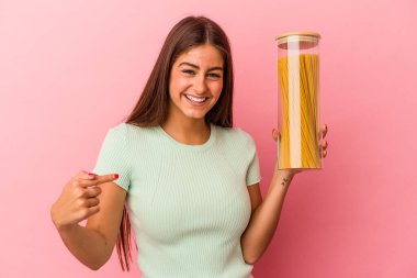 Elinde makarna kavanozu tutan beyaz bir kadın pembe arka planda izole edilmiş, gömlek fotokopi odasını işaret eden, gururlu ve kendinden emin.
