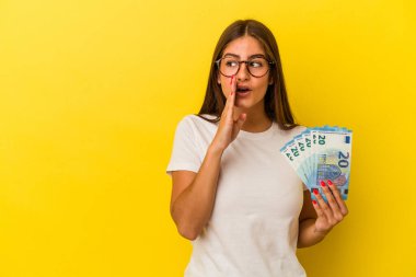 Sarı arka planda izole edilmiş banknotları tutan genç beyaz kadın gizli bir fren haberinin olduğunu söylüyor.