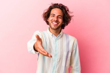 Genç beyaz adam pembe fırında izole edilmiş kameraya elini uzatarak selam veriyor..