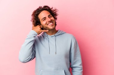 Pembe fırında izole edilmiş genç beyaz bir adam parmaklarıyla bir cep telefonu çağrısı hareketi gösteriyor..