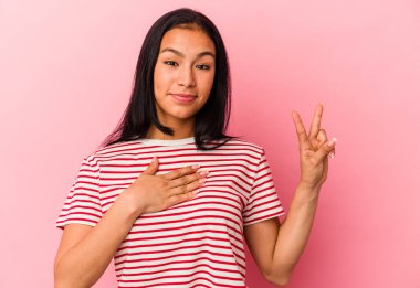 Genç Venezuelalı kadın pembe arka planda izole edilmiş yemin ediyor, elini göğsüne koyuyor..