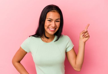 Genç Venezuelalı bir kadın pembe arka planda izole edilmiş, mutlu bir şekilde işaret parmağıyla işaret ediyor..