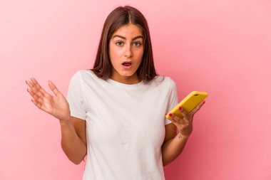 Elinde cep telefonu olan beyaz bir kadın pembe arka planda izole edilmiş. Şaşırmış ve şok olmuş..