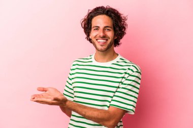 Pembe fırında izole edilmiş genç beyaz bir adam bir palmiye ağacının üzerinde bir kopya alanı tutuyor..