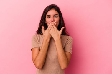 Pembe arka planda izole edilmiş genç beyaz kadın şok olmuş, ağzı ellerle kaplanmış, yeni bir şey keşfetmeye hevesli..