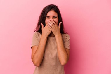 Pembe arka planda izole edilmiş genç beyaz kadın bir şeye gülüyor, elleriyle ağzını kapatıyor..