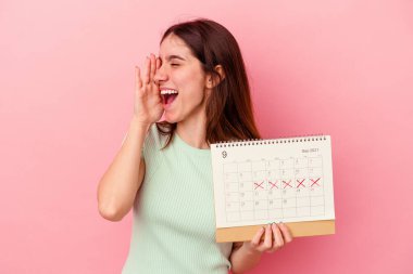Pembe arka planda izole edilmiş takvim tutan beyaz bir kadın bağırıyor ve avuç içini açık tutuyor..
