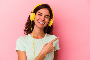 Pembe arka planda izole edilmiş müzik dinleyen beyaz bir kadın gülümsüyor ve boş alanda bir şeyler gösteriyor..