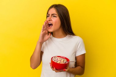 Sarı arka planda izole edilmiş mısır gevreği tutan genç beyaz bir kadın bağırıyor ve ağzı açık bir şekilde avuç içi tutuyor..