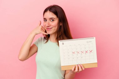 Pembe arka planda takvime izole edilmiş bir takvim tutan genç beyaz kadın parmakları olan bir cep telefonu hareketi gösteriyor..