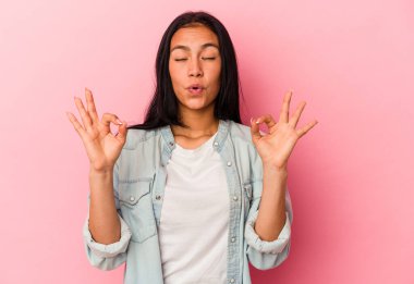 Genç Venezuelalı kadın pembe arka planda izole edilmiş yoğun bir günün ardından dinleniyor, yoga yapıyor..