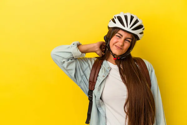 若いです学生の白人女性は 頭の後ろに触れる黄色の背景に隔離された自転車のヘルメットを身に着けています 思考と選択をします — ストック写真