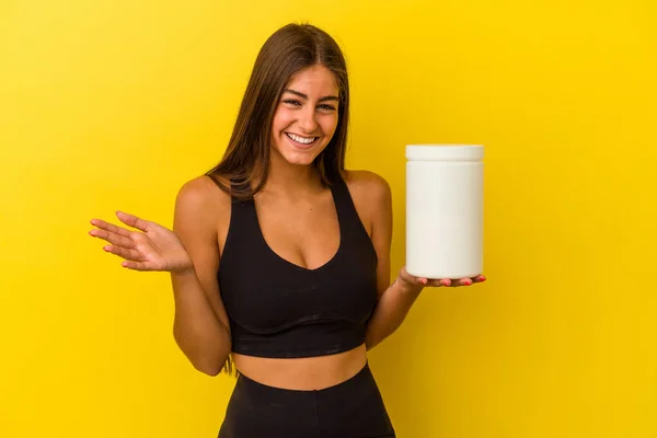 黄色の背景に単離されたタンパク質ボトルを保持若い白人女性は 快適な驚きを受けます 興奮し 手を上げます — ストック写真
