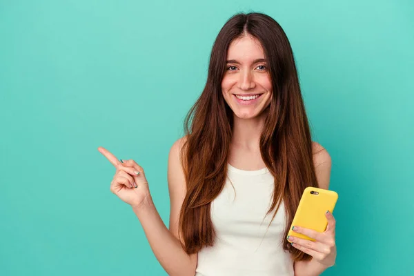 Mladá Běloška Drží Mobilní Telefon Izolovaný Modrém Pozadí Usmívá Ukazuje — Stock fotografie