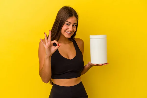 若いですCaucasian女性保持Aタンパク質ボトル隔離された黄色の背景陽気で自信を持ってショーOkジェスチャー — ストック写真