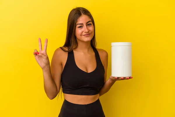 黄色の背景に隔離されたタンパク質ボトルを持っている若い白人女性は 指で2番目を示しています — ストック写真