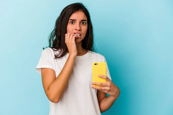 Młoda Biała Kobieta Trzyma Telefon Komórkowy Odizolowany Niebieskim Tle Obgryzając — Zdjęcie stockowe