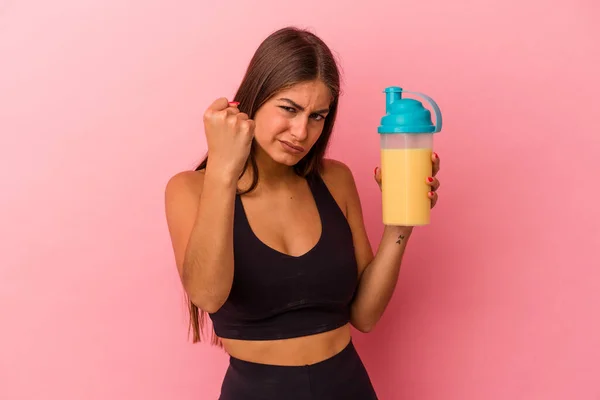 黄色の背景に単離されたタンパク質シェイクを持つ若い白人女性は カメラに拳を示す 積極的な顔の表情 — ストック写真