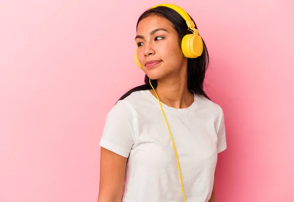 若いベネズエラの女性はピンクの背景に隔離された音楽を聴いて笑顔 陽気で楽しい脇に見えます — ストック写真
