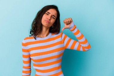 Mavi arka planda izole edilmiş genç beyaz kadın baş parmağını aşağı gösteriyor, hayal kırıklığı konsepti.