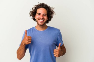 Beyaz arka planda izole edilmiş genç beyaz bir adam iki parmağını da kaldırıyor, gülümsüyor ve kendinden emin..