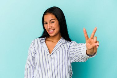 Genç Venezuelalı kadın mavi arka planda iki numarayı parmaklarıyla gösteriyor..