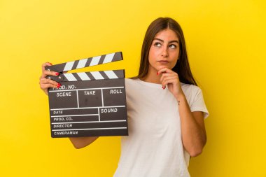 Beyaz arka planda el çırpma tahtası tutan beyaz bir kadın şüpheli ve şüpheci bir ifadeyle yan yana bakıyor..